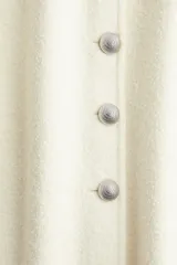 Chaleco largo color crema en punto suave de mezcla de lana. Modelo de corte entallado con ribetes tubulares, escote en V y botones de cúpula metálicos con diseño en relieve.