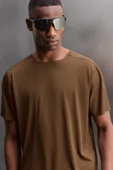 Camiseta deportiva marrón confeccionada en tejido técnico ligero y elástico con estructura perforada. Cuello redondo, manga corta y bajo asimétrico con aberturas laterales. Detalle de logo estampado.