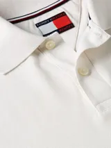 Chomba color crema de piqué de algodón, corte regular, cuello de chomba y cartera de dos botones. Tiene el logo de Tommy Hilfiger bordado en el pecho.
