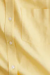 Camisa amarilla de tejido liviano de mezcla de lino y viscosa con cuello, botones adelante y canesú de doble capa con pliegue de caja en la espalda. Modelo de manga larga con bolsillo superior abierto, puños abotonados y bajo redondeado.