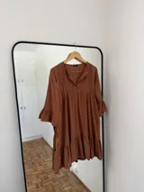 Vestido corto color marrón de fibrana, con cuello mao, tablas en el frente, mangas 3/4 con volados y ruedo con volados.