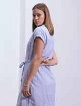 Vestido camisero corto con estampado de rayas verticales celestes y blancas. Tiene cuello camisero, mangas cortas con dobladillo, cierre frontal con botones y cinturón de lazo en la cintura.