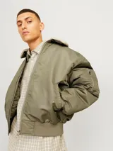 Campera bomber color verde oliva, de manga larga y cuello extendido. Tiene puños ribeteados, cierre con cremallera, bolsillo en la manga y bolsillos frontales con cierre de botón.