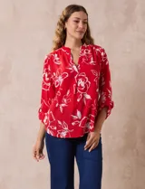 Blusa de gasa roja con estampado floral blanco, cuello a la base con escote en V y mangas 3/4 regulables con presilla y botón.