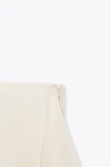 Falda pantalón negra de tiro bajo con cintura drapeada y bajo acabado en volantes superpuestos. Presenta un lazo largo y fino que cae desde el lateral.