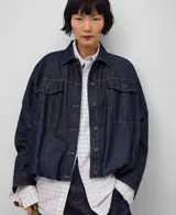 Campera bomber de denim de algodón color azul oscuro, con cuello solapa, manga larga con puño ancho, botonadura frontal, bolsillos con solapa y botón en el pecho, canesú en la espalda y bajo elástico redondeado.
