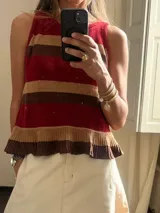 Musculosa de tejido de punto a rayas horizontales en tonos rojo, marrón y beige, con volados en el ruedo.