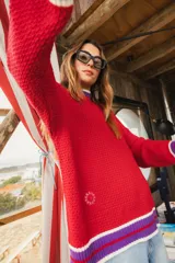 Sweater rojo de punto abierto con cuello redondo y mangas largas. Presenta detalles en puños, cuello y ruedo en contraste blanco, lila y rojo.