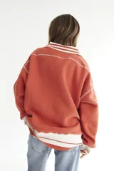Buzo celeste con cuello polo y puños en rib color verde lima. Tiene un parche con el logo de la marca en el pecho y rayas horizontales en el ruedo.