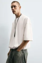 Camiseta blanca de algodón, corte holgado, cuello redondo, manga corta y bajo con elástico interior.