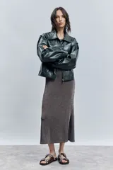 Cazadora corta de efecto piel color verde oscuro, con cuello solapa, cierre frontal de cremallera y mangas largas abullonadas con puños elásticos.