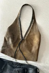 Top marrón de cuero ovino vintage con cuello halter y espalda descubierta. Presenta detalle artesanal de cutouts y pasamanería en negro alrededor del cuello y lazos finos negros para atar en el frente.