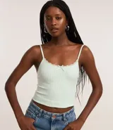 Top ajustado de tejido seamless (sin costuras) color verde menta pálido, con escote redondo ribeteado con encaje blanco y un pequeño moño decorativo en el centro.