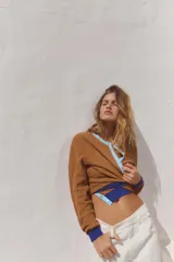 Chaqueta marrón de punto con cuello redondo y manga larga. Presenta cierre frontal con botones y detalles color block en azul en cuello, puños y ruedo.