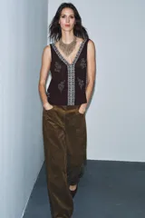 Top sin mangas color negro con escote pico profundo. Presenta bordados florales y un panel central con diseño geométrico, ambos realizados con aplicación de abalorios plateados o blancos.