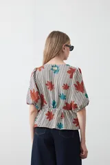 Blusa de silueta relajada con estampado de lunares negros sobre fondo crema. Cuenta con escote en V con lazos regulables, frunce bajo el busto y mangas cortas con volumen.