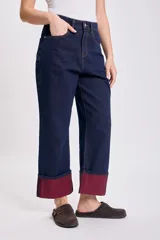 Pantalón de jean azul oscuro, de corte recto y holgado, con el bajo doblado mostrando un forro color bordó.