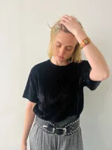 Blusa negra de terciopelo plisado con mangas cortas y cuello redondo.