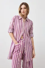 Vestido camisero a rayas verticales fucsia y blanco, con cuello camisero, mangas 3/4 con puños abotonados y cierre frontal con botones.