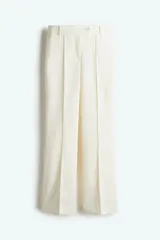 Pantalón acampanado color crema, de tiro bajo, con cierre y pretina prolongada con un botón oculto y uno visible. Modelo con bolsillos laterales discretos, bolsillos atrás insertados y piernas extralargas acampanadas con pliegue cosido adelante y planchada atrás.