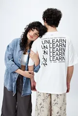 Remera blanca de corte amplio con mangas cortas y estampado con la frase "Unlearn" en el frente y gráfico en la espalda.