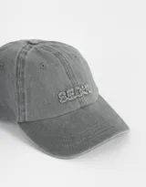 Gorra de béisbol azul denim con efecto lavado y bordado frontal con la palabra "Tokyo" en blanco. Ajuste trasero con hebilla metálica.