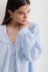 Camisa celeste de algodón con bordado calado, cuello en V y mangas largas abullonadas con puños elásticos.