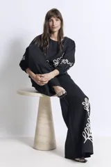 Pantalón negro de corte palazzo con apliques bordados en color crema en la parte inferior de una pierna.