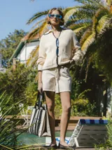 Cardigan tejido color crema con cuello polo, cierre con botones y ribete negro en cuello, puños y ruedo.