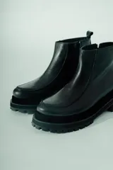 Bota corta de cuero negro, estilo botín chelsea, con puntera cuadrada y suela track gruesa y robusta.