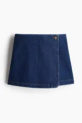 Short pollera cruzado de tiro alto en sarga de algodón color azul denim con botón a un lado, cierre oculto adelante y bolsillos insertados decorativos atrás.