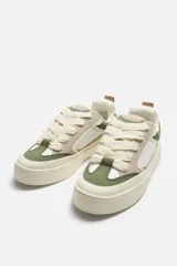 Zapatillas deportivas tipo skate, color blanco, beige y verde. Parte superior fabricada en combinación de piezas y materiales. Detalle de cordones maxi y suela con volumen.