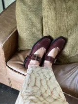 Zapatos de cuero color marrón con punta cuadrada, tira sobre el empeine con hebilla dorada y suela plana.