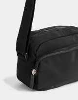 Bandolera negra de tela deportiva con bolsillo frontal con cierre, correa regulable y tag de goma.