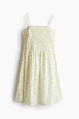 Vestido corto blanco con estampado de flores amarillas, de algodón, con breteles finos y cuerpo fruncido.
