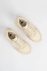 Zapatillas acordonadas color beige con suela blanca y detalles en marrón claro.
