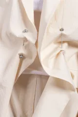 Blazer color crema de corte amplio con diseño asimétrico y detalle de nudo frontal.