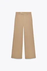 Pantalón de vestir color beige, de tiro alto y pierna ancha. Cierre frontal con cremallera, botón interior y gancho metálico.