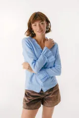 Blusa blanca de lino con botones de nácar, volados en el escote y mangas largas con puños acampanados. Corte recto y holgado.