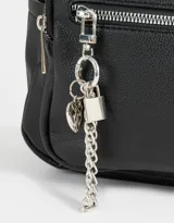 Mochila urbana negra de cuerina con bolsillo frontal con cierre y charm colgante de cadena con dije de corazón y candado. Tiene correas regulables, manija superior, cierre superior, doble bolsillo frontal (uno con charm metálico) y bolsillos laterales.