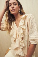 Blusa color crema con diseño calado, escote en V y volados frontales. Tiene mangas 3/4 con puños elastizados y cierre frontal con botones.