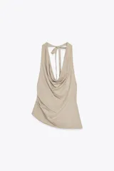 Top color beige confeccionado en algodón 100% con efecto teñido. Presenta cuello halter con lazada y escote drapeado. El bajo tiene un acabado asimétrico.