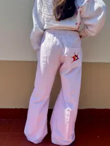 Pantalón de algodón con motivo de rayas verticales finas en tonos rosado y blanco. Presenta cintura elastizada, bolsillos delanteros y un bolsillo trasero tipo plaque con un bordado de pájaro estilizado en tonos naranja y marrón. El calce es recto y ancho.