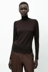 Jersey negro de punto liso con cuello alto, manga larga y detalle de botones dorados en los puños.