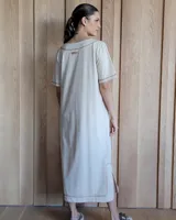 Vestido midi negro con cuello redondo y mangas cortas. Presenta dos bolsillos cuadrados en el pecho y ribetes blancos en cuello, mangas, bolsillos y ruedo.