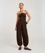 Mono largo de estilo Aladim, color marrón oscuro, con escote halter y busto fruncido. El pantalón es ancho y termina ajustado en los tobillos.