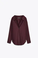 Camisa color borgoña de Zara Woman Collection, confeccionada en algodón popelín. Tiene cuello solapa, escote en pico, mangas largas con puños abotonados, bajo redondeado y cierre frontal con botones.