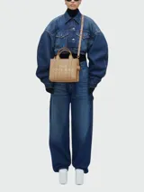 Bolso tote pequeño de cuero texturizado color gris con doble asa corta superior y correa larga extraíble y ajustable para llevar al hombro. Estampado frontal con el texto "The Tote Bag" y el nombre de la marca.