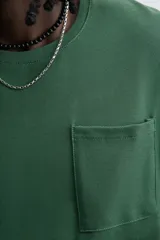 Camiseta verde oscuro de corte relaxed fit, cuello redondo, manga corta y bolsillo plastrón en el pecho.