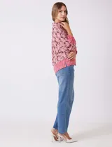 Camisa de gasa con cuello con solapa y apertura central con botones. Presenta un estampado de patrones geométricos en tonos rosados, marrones y crema, con un borde inferior en un patrón geométrico más denso en tonos rojizos/rosados. Las mangas son amplias de largo tres cuartos con puño elastizado.